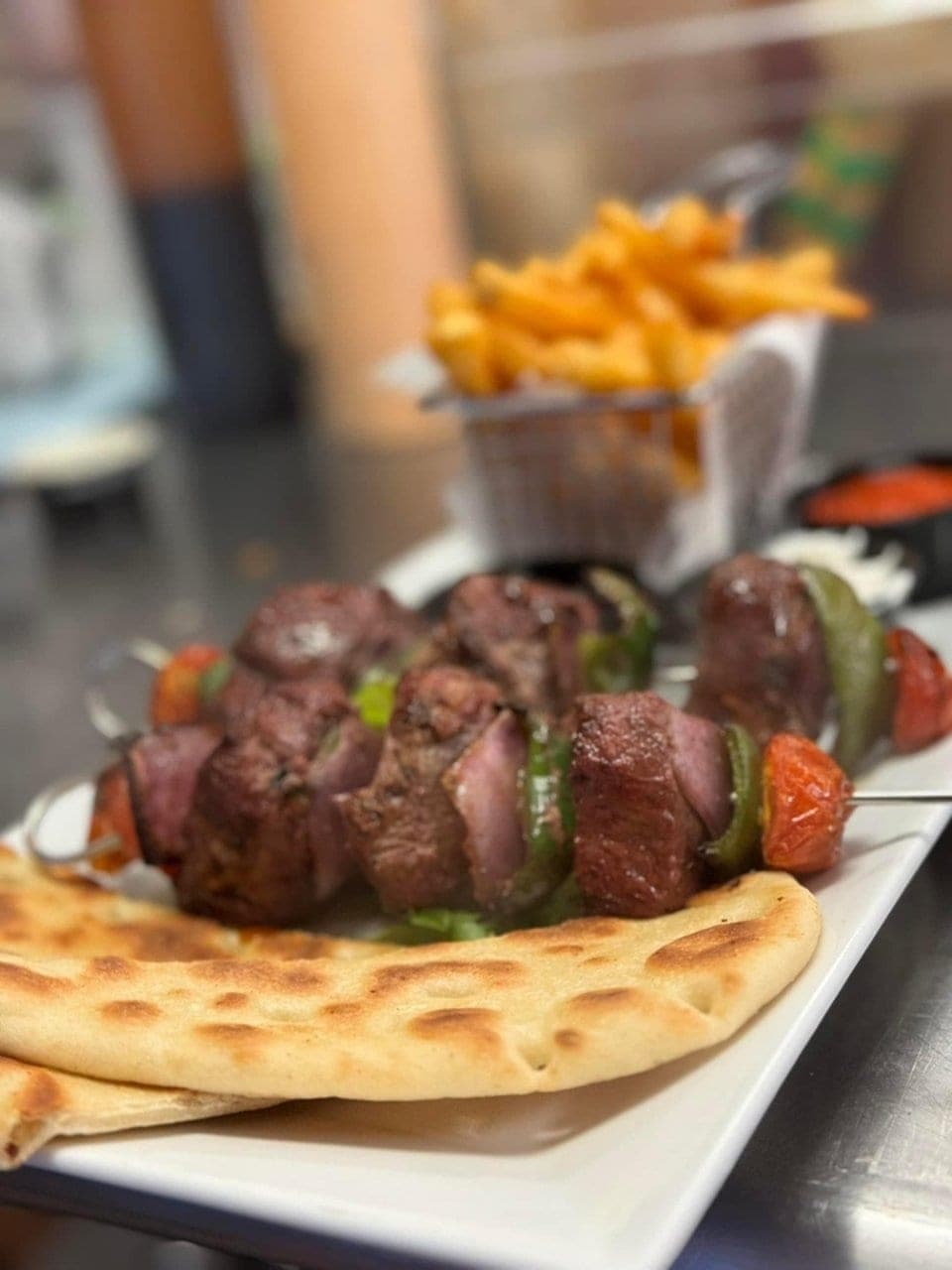 Grilled meat and vegetable skewers over flatbread with fries at Titos Lounge