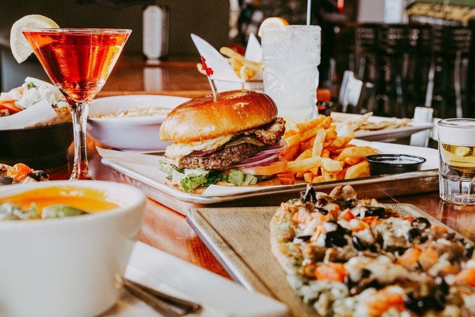 A spread at Titos Lounge with a burger, fries, flatbread, soup, and cocktails