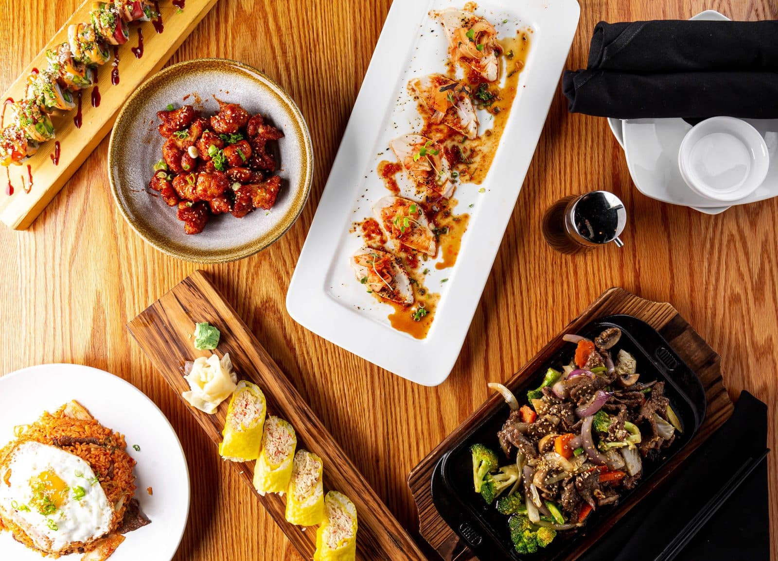 Overhead spread of sushi rolls, sashimi, and sizzling plates at Wasabi Ankeny